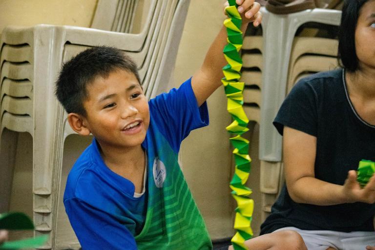 Smiling child holding up his green and yellow paper spring.