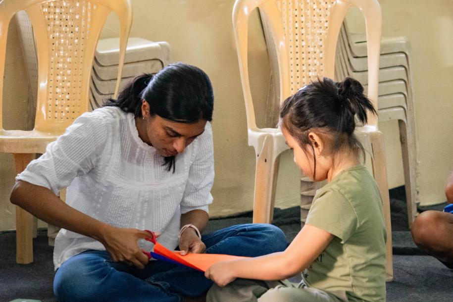 LML volunteer helping child make a paper spring.